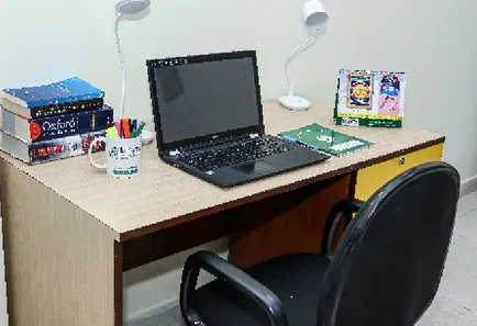 A study desk in a DWPS hostel room, with a lamp, a laptop and a stack of books