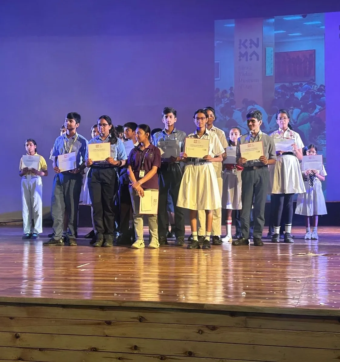 Students on stage holding their certificates at the inter-school art battle